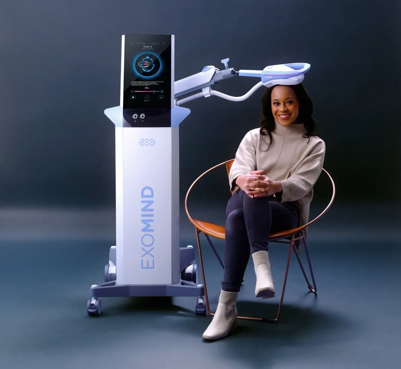 Client seated next to the ExoMind device demonstrating treatment positioning