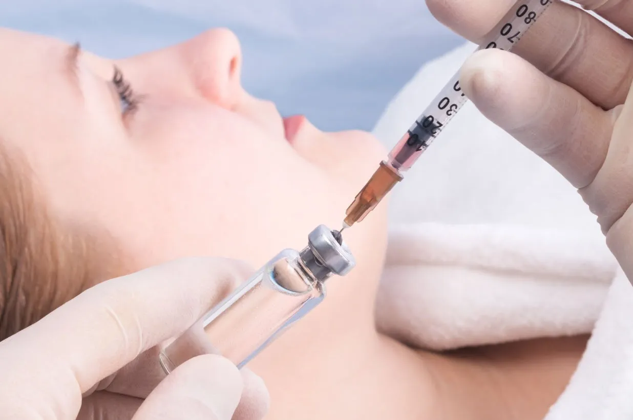 A medical professional wearing gloves prepares a syringe by drawing liquid from a vial, with a patient lying down in a clinical setting, illustrating a safe and controlled medical procedure, which raises the question: is peptide therapy safe for various health and wellness treatments?