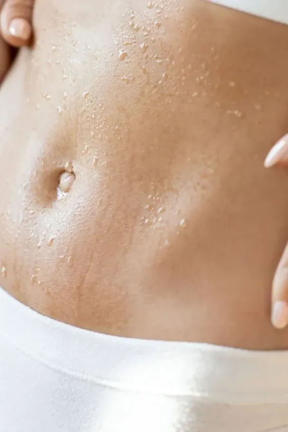 Close-up of a woman's toned midriff beaded with water, above a white waistband